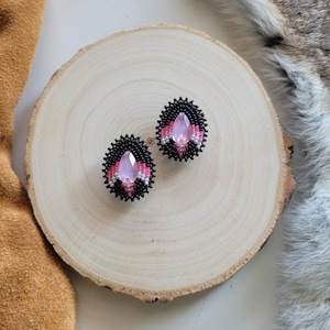 Pode incluir: Um par de brincos de contas pretas e rosa com um cristal rosa em forma de lágrima no centro.