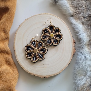 May include: A pair of black and gold beaded flower earrings with a gold centre. The earrings are on a wooden surface.