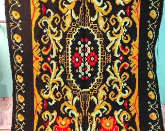 May include: A black rug with a floral pattern in shades of yellow, red, and green. The rug has a border of yellow and green flowers.