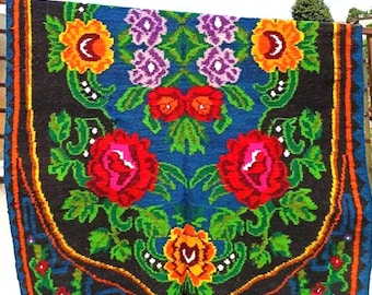 May include: A colorful handwoven rug with a floral pattern. The rug features red, pink, orange, yellow, green, purple, and blue flowers on a dark blue background. The rug has a black border with a fringe.