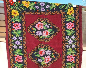 May include: A red rug with a floral pattern. The rug has a dark border with yellow, pink, and purple flowers. The centre of the rug has two large floral designs.