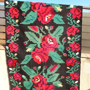 Puede incluir: Una alfombra de lana negra con un diseño tradicional rumano con rosas rojas y hojas verdes.