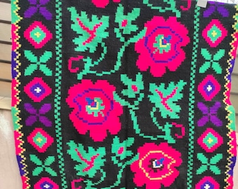 May include: A black woven rug with a floral pattern in shades of pink, green, yellow, and purple. The rug has a fringe border.