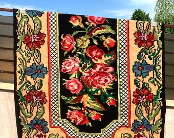 May include: A vintage floral rug with a black centre panel featuring a bouquet of pink, red, and green roses. The rug has a cream background with a black and white chequered border and floral designs in shades of red, pink, blue, green, and yellow.