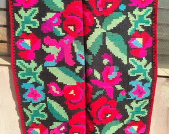 May include: A traditional Romanian handwoven rug with a floral pattern. The rug is black with red, pink, green, and blue flowers. The rug is made of wool and has a fringe border.