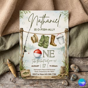 以下が含まれることがあります： 釣りテーマの招待状。招待状には「Nathaniel」という名前と「IS O-FISH-ALLY ONE」というフレーズが記載されています。釣り竿、ベスト、ブーツ、浮きが含まれています。「Take the bait and join us!」というテキストも表示されています。