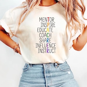 Puede incluir: Camiseta color crema con las palabras "MENTOR, INSPIRE, EDUCATE, COACH, SHARE, INFLUENCE, INSTRUCT" en negro. La palabra "EDUCATE" es verde, "COACH" es amarilla, "SHARE" es azul e "INFLUENCE" es morada.