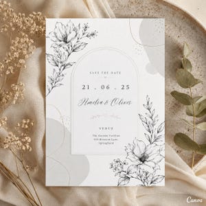 Peut inclure: Une carte Save the Date blanche avec un cadre en arche central, des illustrations florales noires au trait et le texte : SAVE THE DATE, 21.06.25, Amelia & Oliver, VENUE, The Garden Pavilion, 456 Blossom Lane, Springfield, avec des formes grises.