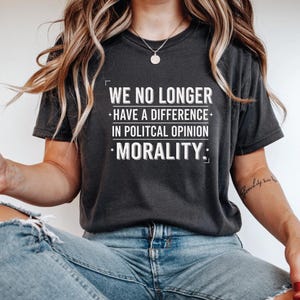 Peut inclure: T-shirt gris foncé avec le texte "WE NO LONGER HAVE A DIFFERENCE IN POLITICAL OPINION: MORALITY." Le t-shirt est de style décontracté, adapté au quotidien. Le texte est en blanc gras.