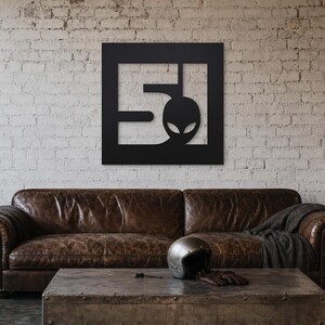 A metal sign depicting the number 51 and a head of a stylised alien, square shape and black colour.
