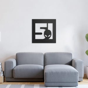 A metal sign depicting the number 51 and a head of a stylised alien, square and black in colour.