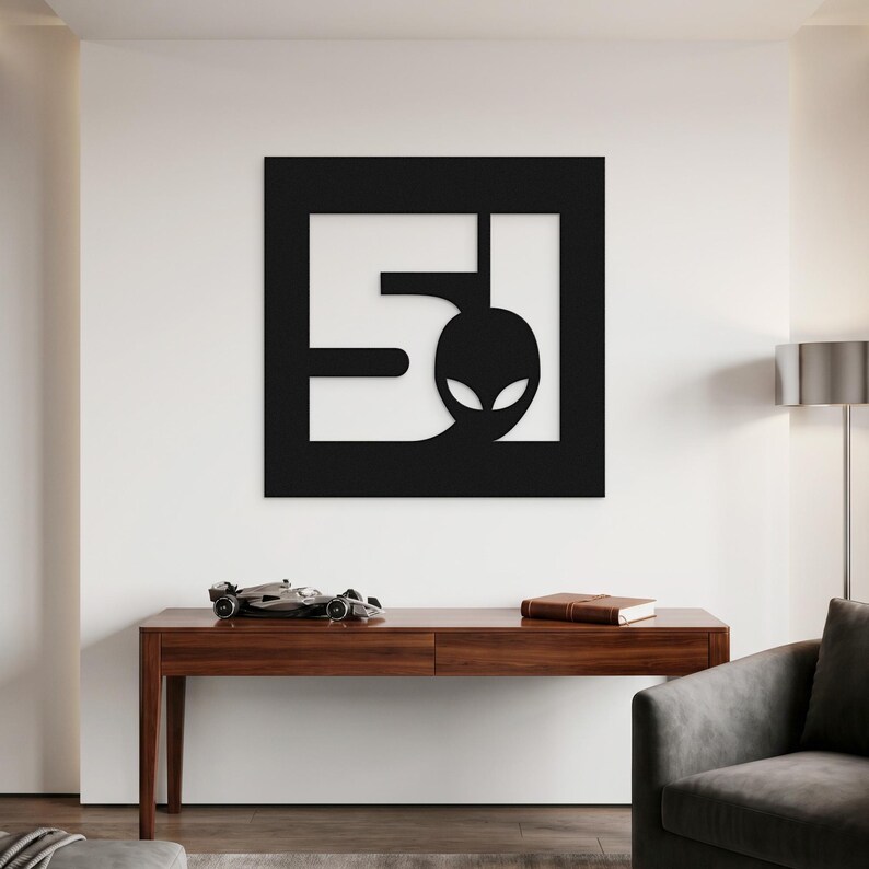 A metal sign depicting the number 51 and a head of a stylised alien, square shape and black colour.