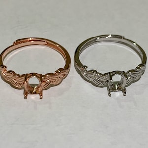 May include: Two adjustable rings with a leaf design. One ring is rose gold and the other is silver. Both rings have a blank oval setting in the center.