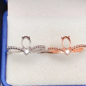 May include: Two rings with a prong setting for an oval stone. The ring on the left is silver and the ring on the right is rose gold. Both rings have a small round stone set in the band.
