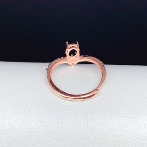 May include: A rose gold ring with a round setting for a stone. The ring has a delicate band with small stones around the setting.