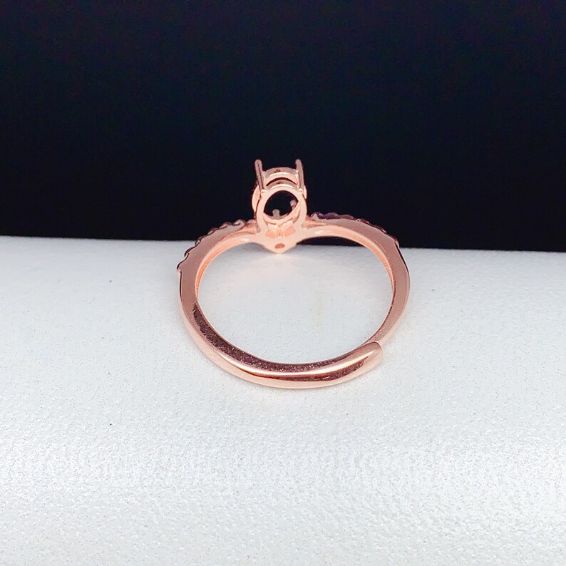 May include: A rose gold ring with a round setting for a stone. The ring has a delicate band with small stones around the setting.