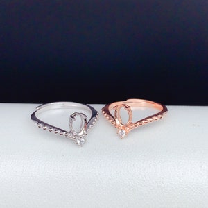 May include: Two rings with a V-shaped design. The ring on the left is silver with a clear stone. The ring on the right is rose gold with a clear stone.