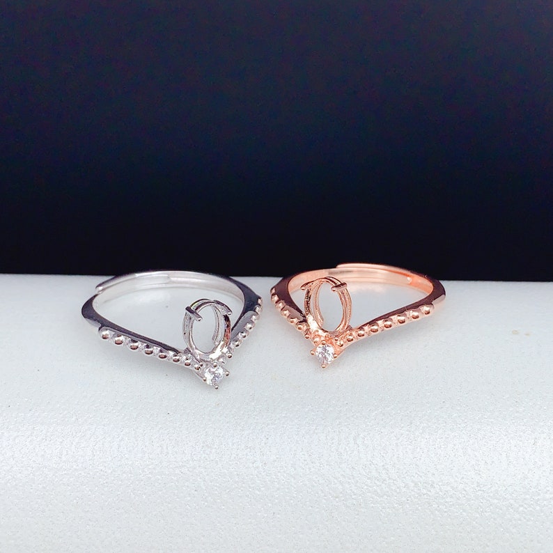 May include: Two rings with a V-shaped design. The ring on the left is silver with a clear stone. The ring on the right is rose gold with a clear stone.