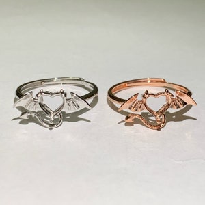 Puede incluir: Dos anillos con un diseño en forma de corazón con alas y cola. El anillo de la izquierda es de plata y el anillo de la derecha es de oro rosa.