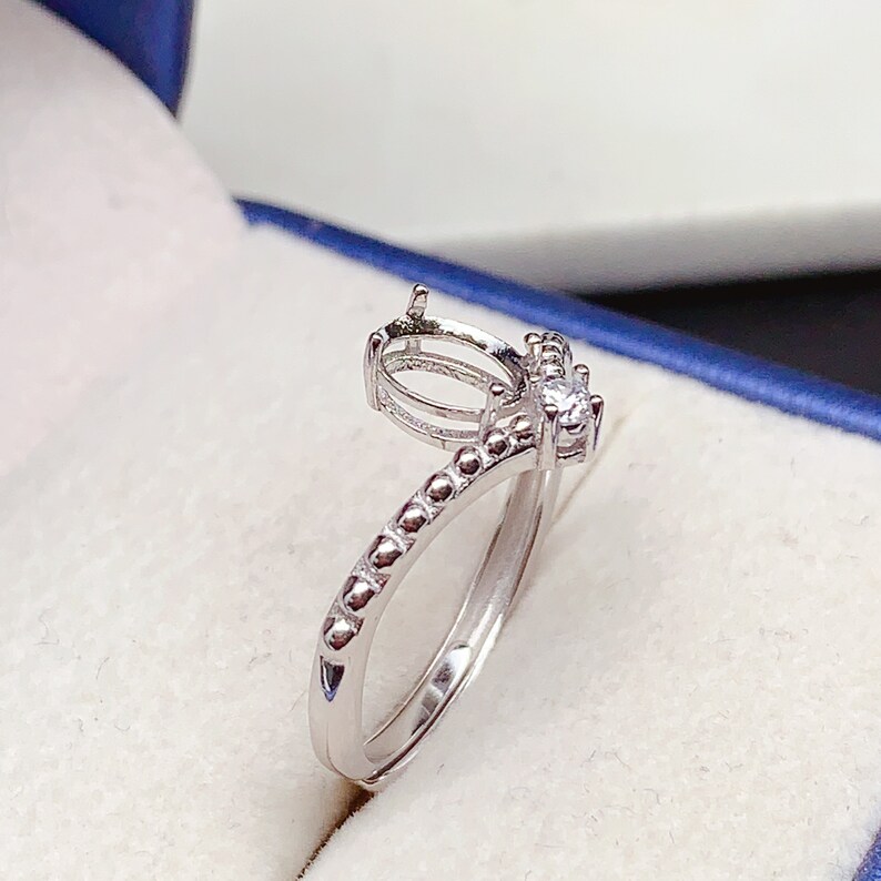 May include: A silver ring with a bezel setting for an oval stone. The ring has a beaded band and a small clear stone on the side.
