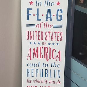 May include: A white wooden sign with blue and red text. The sign reads "I pledge allegiance to the flag of the United States of America and to the republic for which it stands one nation under God indivisible with liberty and justice for all".