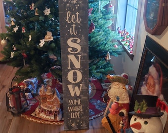 Puede incluir: Un letrero de madera azul con letras blancas que dice "Let it Snow Some Where Else". El letrero está decorado con copos de nieve. El letrero está delante de un árbol de Navidad con adornos y un muñeco de nieve.