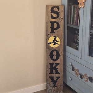 Peut inclure: Un grand panneau rectangulaire en bois avec une finition brune patinée. Le mot SPOOKY est imprimé verticalement en grandes lettres noires. Un graphique de lune circulaire jaune avec une silhouette noire de sorcière sur un balai remplace le O.