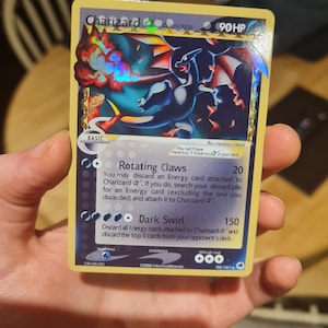 May include: A Charizard Pokémon trading card. The card features a blue and red dragon-like creature with the text "Charizard" at the top. The card has a yellow border and includes text describing the creature's abilities and stats.