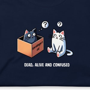 Könnte beinhalten: Ein marineblaues T-Shirt mit einer Cartoon-Illustration einer Katze in einer Schachtel mit der Aufschrift "Schrödingers Katze" und einer anderen Katze, die mit Fragezeichen über dem Kopf verwirrt aussieht. Der Text "DEAD, ALIVE AND CONFUSED" ist unter der Illustration aufgedruckt.