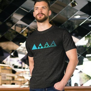 Puede incluir: Una camiseta de manga corta en color gris carbón con un estampado gráfico de cuatro triángulos de color turquesa dispuestos en fila. El diseño muestra un patrón fractal, donde cada triángulo sucesivo presenta mayor complejidad.