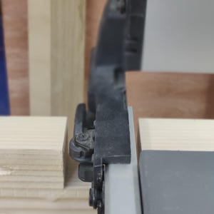 May include: Close-up of a black and silver window sash with a black plastic latch. The sash is attached to a wooden frame.