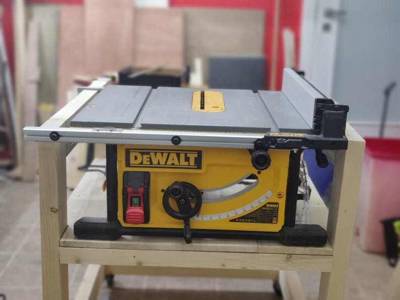 May include: A yellow and black DeWalt table saw with a gray table top and a black fence. The saw is sitting on a wooden stand with two shelves.