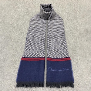 May include: A gray and white patterned scarf with navy blue ends. The scarf has red stripes near the navy blue ends and the words "Christian Dior" are embroidered on the navy blue section. The scarf has a fringed edge.