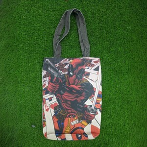 Op de afbeelding: Een zwarte canvas tote bag met een rood en zwart Deadpool-personage ontwerp. Het ontwerp toont Deadpool met een pistool en een zwaard, met speelkaarten op de achtergrond.