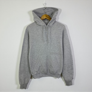 Puede incluir: Una sudadera con capucha gris jaspeado con un bolsillo de canguro. La sudadera con capucha está colgada de una percha de madera sobre un fondo blanco. La sudadera tiene mangas largas y una capucha con cordón.