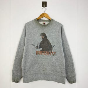 May include: A grey sweatshirt with a Godzilla graphic, the Golden Gate Bridge, and the orange text "RODNEZILLA". It has a crew neck and long sleeves. The Fruit of the Loom label is visible on the collar.