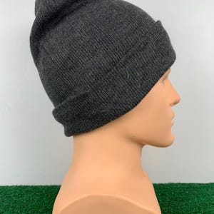 Puede incluir: Un gorro de punto de color gris oscuro. El gorro est&aacute; doblado en la parte superior y tiene un dise&ntilde;o sencillo.