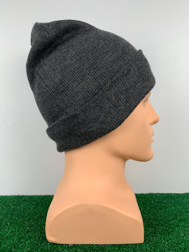 Puede incluir: Un gorro de punto de color gris oscuro. El gorro est&aacute; doblado en la parte superior y tiene un dise&ntilde;o sencillo.