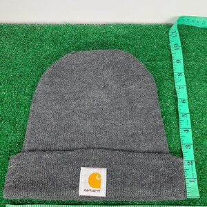 Puede incluir: Gorro de lana gris con un parche del logotipo de Carhartt. El logotipo es amarillo con un contorno negro y la palabra "carhartt" en blanco.