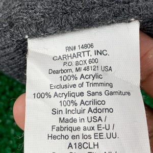 Puede incluir: Una etiqueta blanca con texto negro sobre un fondo gris. La etiqueta dice "RN# 14806 CARHARTT, INC. P.O. BOX 600 Dearborn, MI 48121 USA 100% Acrylic Exclusive of Trimming 100% Acrylique Sans Garniture 100% Acrilico Sin Incluir Adorno Made in USA / Fabrique aux E-U/ Hecho en los EE.UU. A18CLH One Size Fits All / Taille Universelle / Unitalla"