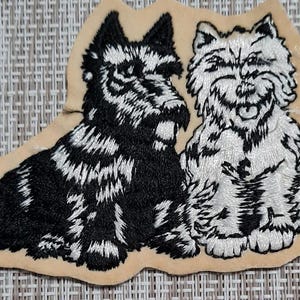 May include: Embroidered patch featuring two dogs, one black and one white, with a beige background.