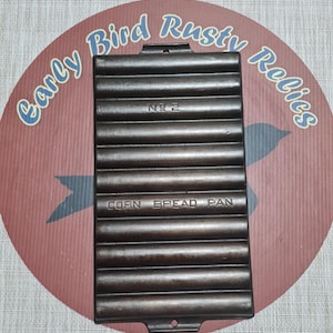 May include: A cast iron corn bread pan with a rectangular shape and ridged interior. The pan is marked "No 2" and "Corn Bread Pan". The pan is dark brown and sits on a red and brown background with the text "Early Bird Rusty Relics".