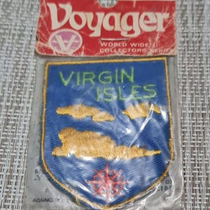 May include: A blue and gold embroidered patch with the text "Virgin Isles" in green letters. The patch is in a plastic bag with a red and white "Voyager" label.
