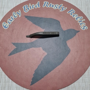 May include: A dark brown Quick Mead bottle stopper on a round, red and brown background with a blue bird silhouette and the text "Early Bird Rusty Relics" in a curved font.