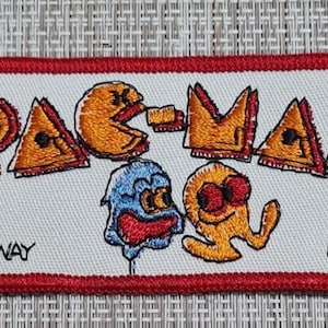 May include: Embroidered Pac-Man patch with a red border. The patch features the Pac-Man logo and characters in orange, yellow, blue, and red. The text "MIDWAY" and "©1981" are also visible.