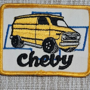 May include: A yellow embroidered patch with a vintage Chevy van and the word "chevy" in black cursive lettering.
