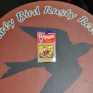 May include: A package of Appalachian Trail fishing tackle from the Voyager World Wide Collection Series. The package is on a brown, circular sign with the text "Early Bird Rusty Relics" in blue and a black bird silhouette.