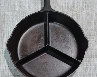 May include: A black cast iron skillet with three divided sections. The skillet has a loop handle.