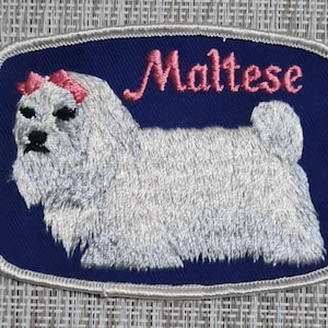 May include: Embroidered patch featuring a white Maltese dog with pink bows on a dark blue background. The text "Maltese" is embroidered in pink above the dog.