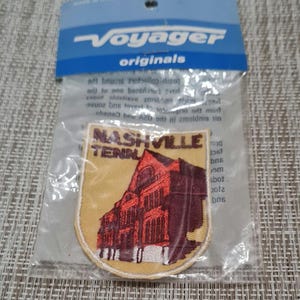 May include: A yellow and red embroidered patch with the text "Nashville Tenn" and a red building with white windows. The patch is packaged in a clear plastic bag with a blue and white Voyager Originals header.